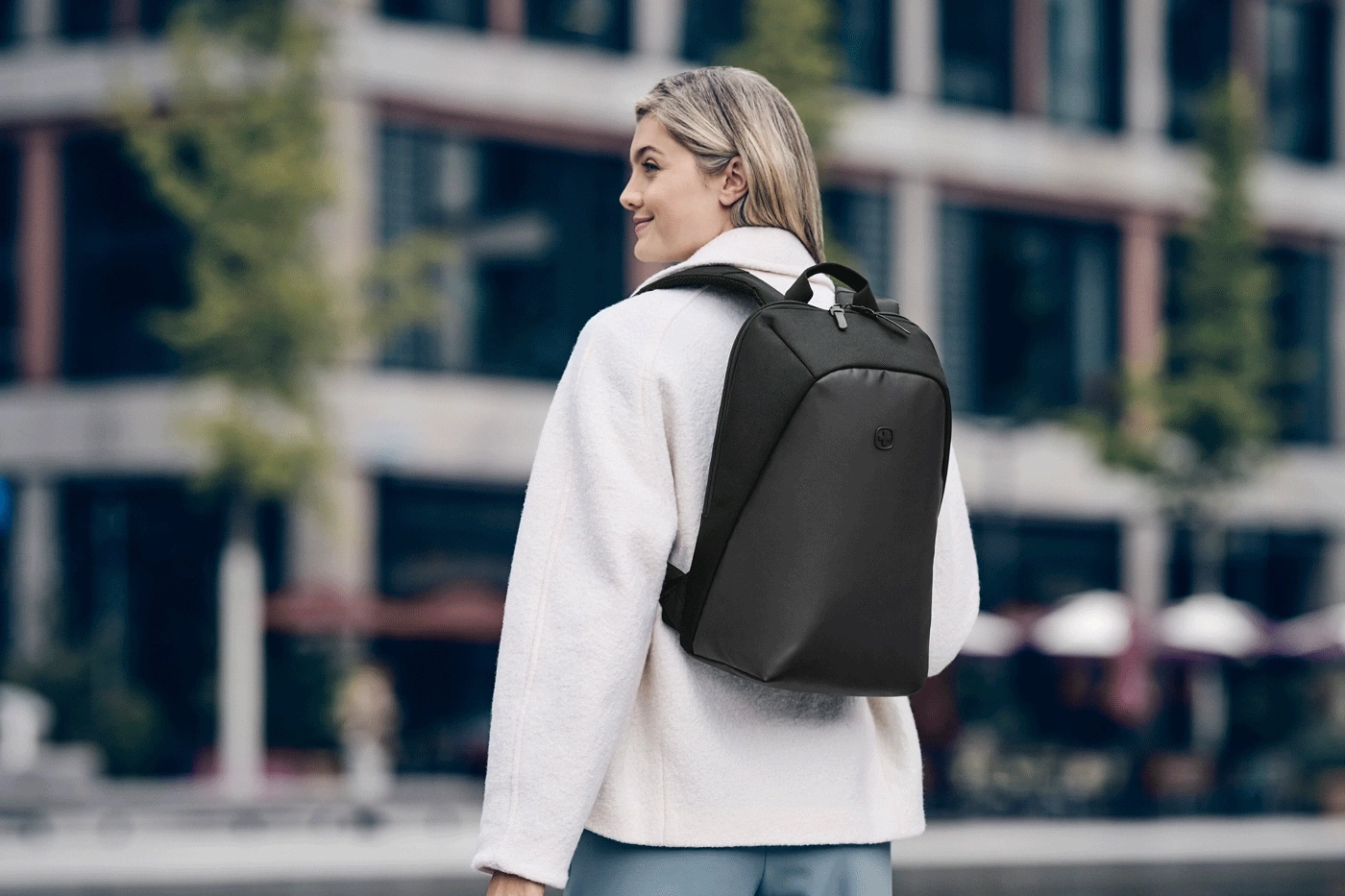 Woman with a black backpack on her back, standing in front of a building.
