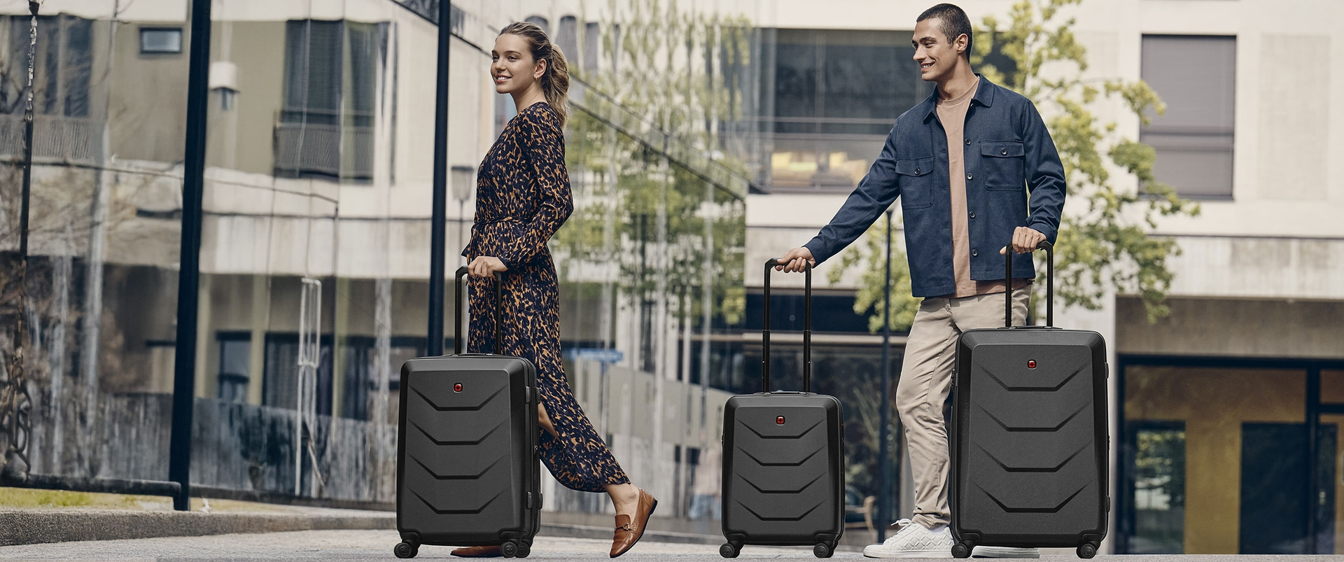 A couple with luggage in front of a building. They are smiling.