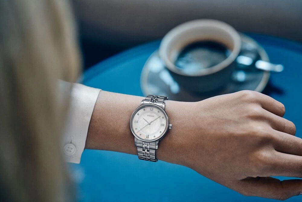 Frau mit Uhr und Kaffee, die auf eine blaue Tischplatte blickt.