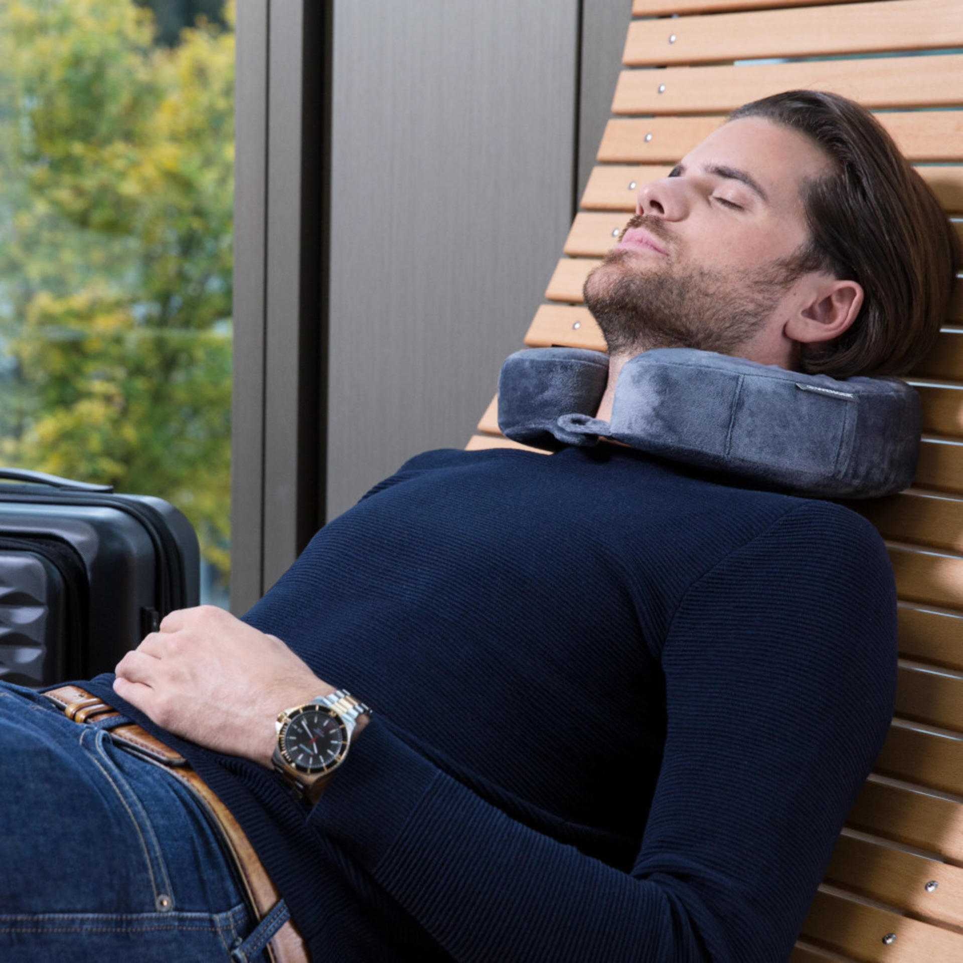 Man sleeping with neck pillow on wooden recliner by window