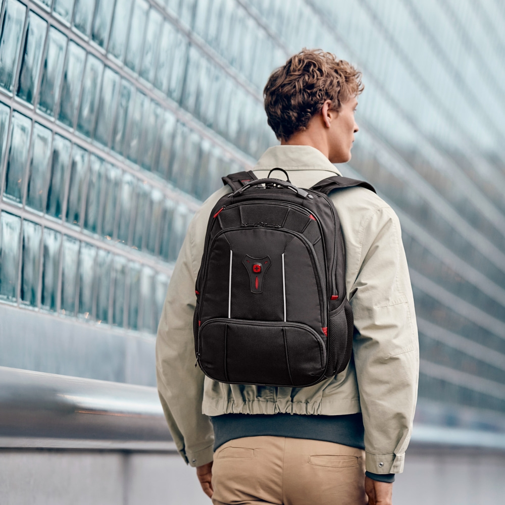 Man with backpack in front of glass facade, looking sideways, cityscape, modern