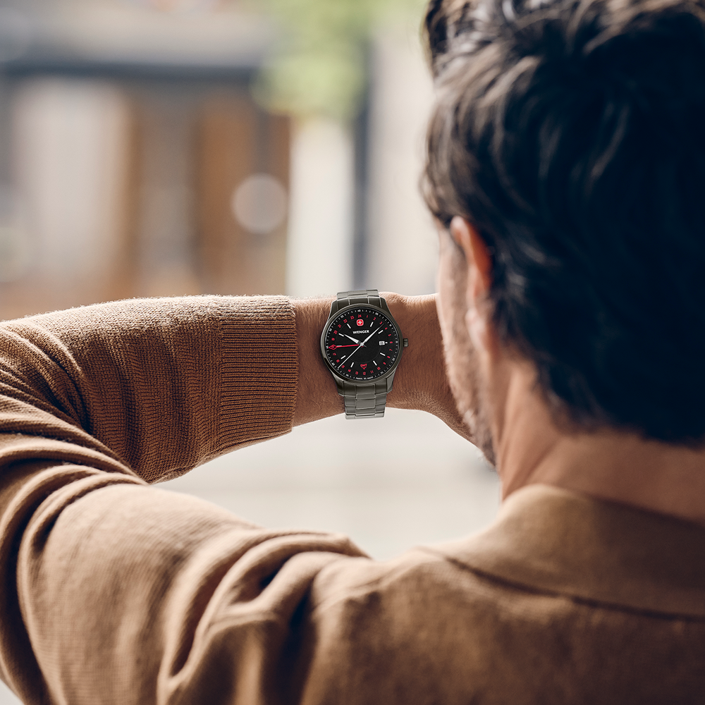 A man checks his watch while wearing a brown shirt.