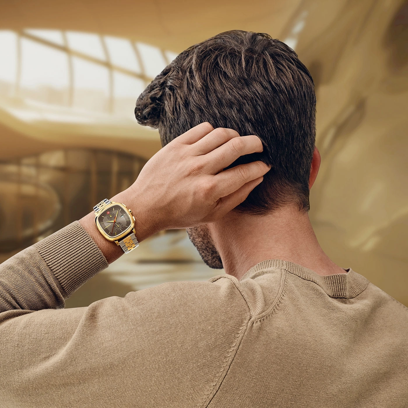 Man scratching his head, wearing a watch, in a modern building, back view