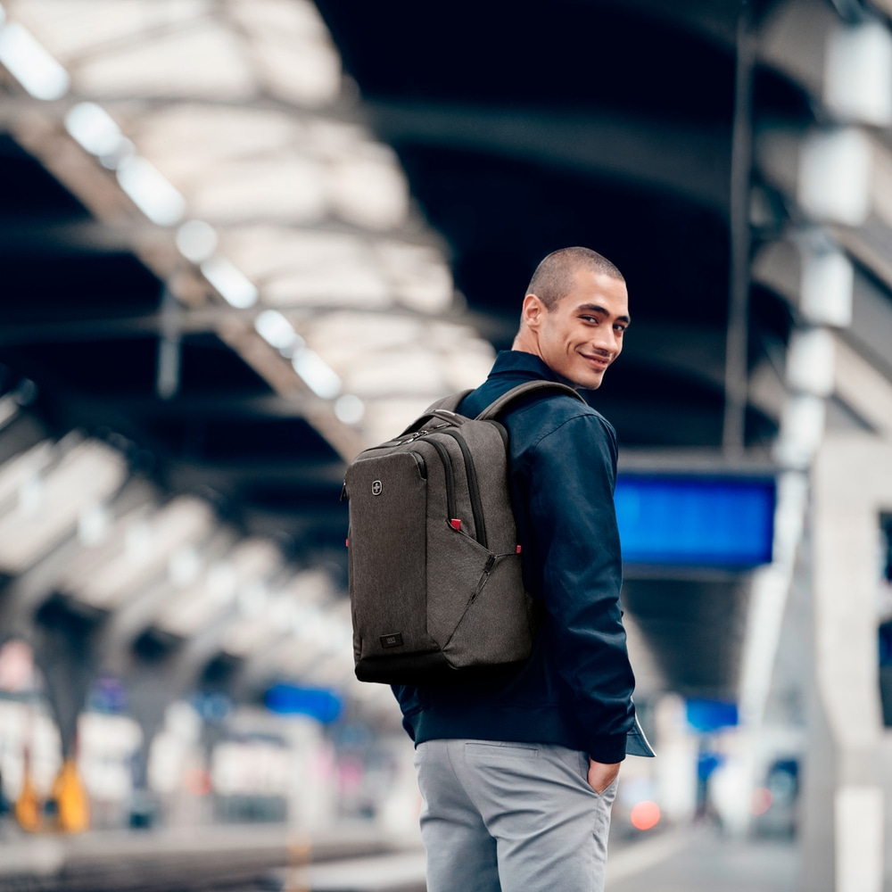 Man with backpack looking back and smiling at a train station platform.